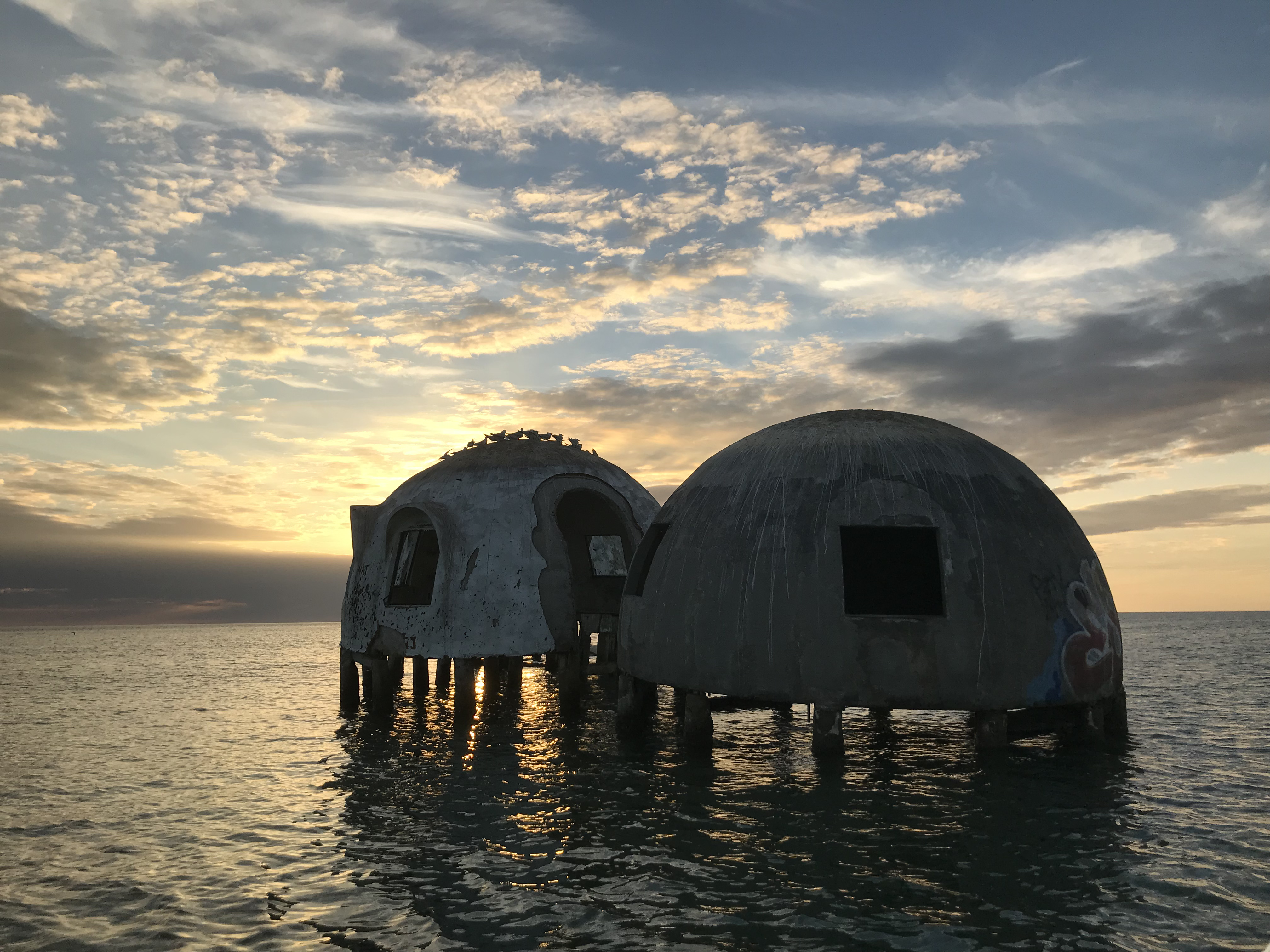 the top of a nearly submerged home peaking out of the water in the sunset